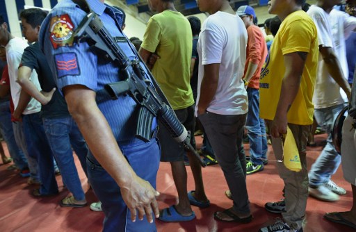MASS SURRENDER. A Philippine policeman stands guard as people line up to register with the police during the mass surrender of some 1,000 alleged drug users and pushers in the town of Tanauan, Quezon. AFP PHOTO / TED ALJIBE 