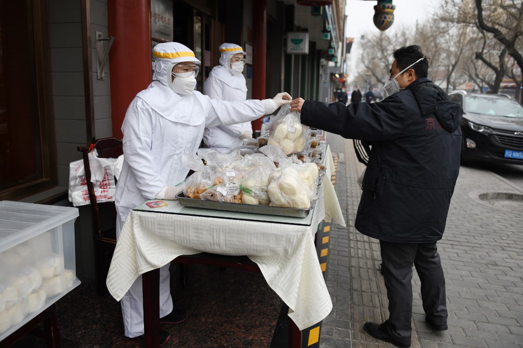 PROTECTIVE CLOTHING. A restaurant worker, dressed for protection against the novel coronavirus, hands over a bag of food to a customer outside their restaurant in Beijing, China, on February 20, 2020. Photo by Greg Baker/AFP 