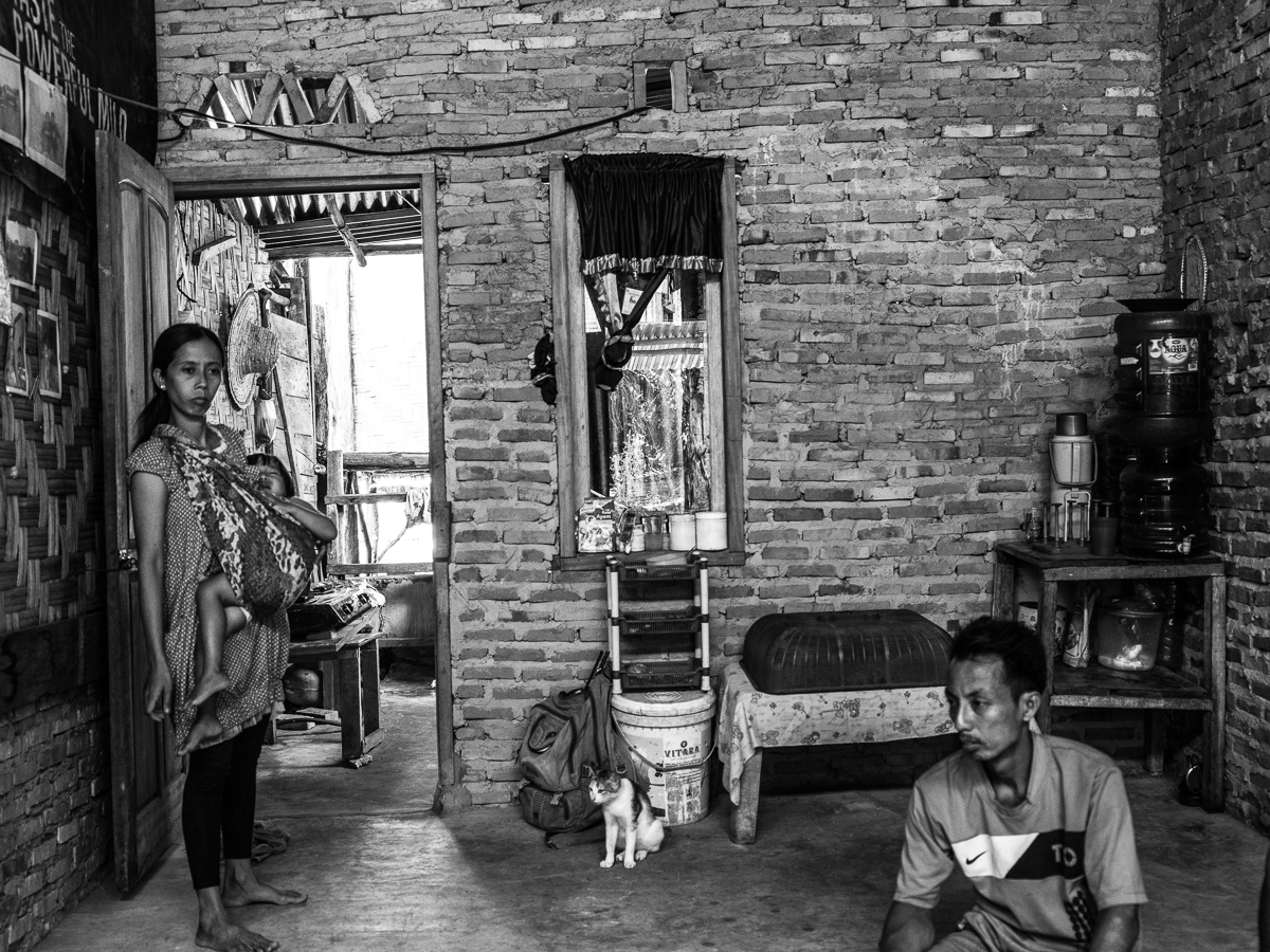 AFTER A DAY'S LABOR. Ida tries to comfort her daughter Santi while her husband Supriyono sits on the floor after a day's work. The gallon jugs of water in the corner are their only water for two weeks. They pay 56,000 Rupiah ($3.84) per gallon.  