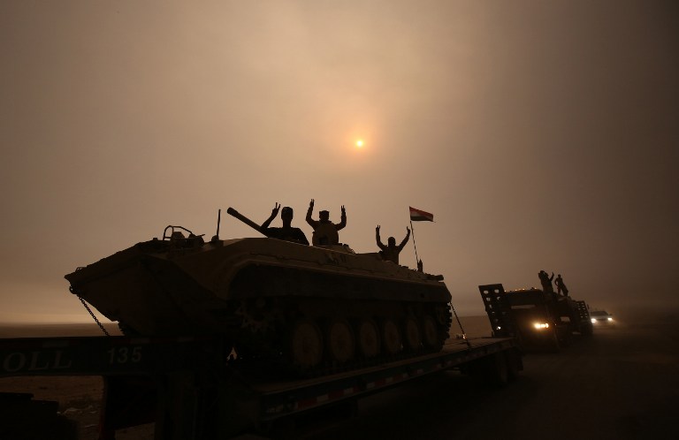 MOSUL OFFENSIVE. Iraqi forces flash the V-sign as they stand on an infantry fighting vehicle loaded on a truck driving through the Al-Shura area, south of Mosul, on October 24, 2016. Photo by Ahmad al-Rubaye/AFP 
