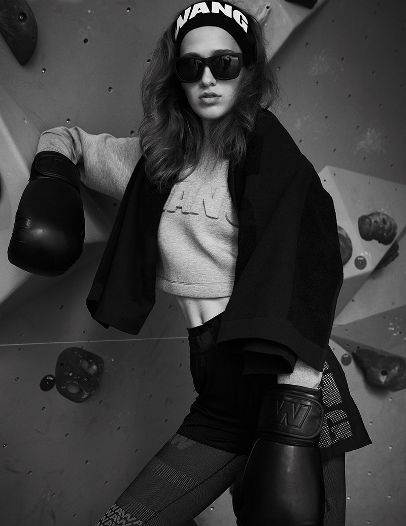 Jovana S. wears: Gray cropped ‘WANG’ sweater with mesh shorts over black and gray leggings. Boxing gloves, shades and body towel