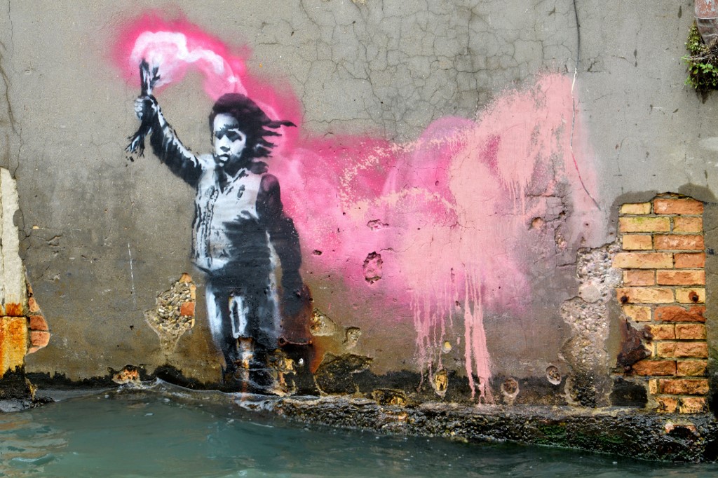 MIGRATION. An alleged work by British street artist Banksy depicting a migrant child wearing a lifejacket holding a pink flare, is painted on the outer wall of a house overlooking the canal Rio de Ca Foscari, in Venice, on May 21, 2019. Photo by Marco Sabadin/AFP 