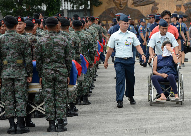 A grieving relative of one of the slain SAF member is wheeled past flag-draped coffins during a heroes' welcome at the Villamor Airbase in Pasay City on January 29, 2015. Photo by Ted Aljibe/AFP 