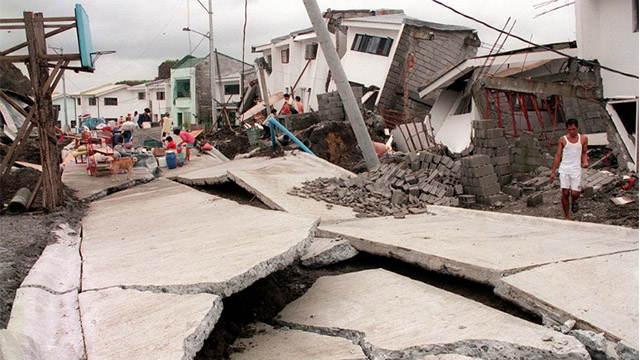 A man looks at a cracked road running past collapsed houses in the Cherry Hills residential subdivision of suburban Antipolo 04 August 1999 following a landslide. At least 10 people were killed and up to 47 others remain missing after several days of heavy monsoon rains triggered the deadly landslide. Photo of AFP Photo/Romeo Gacad 