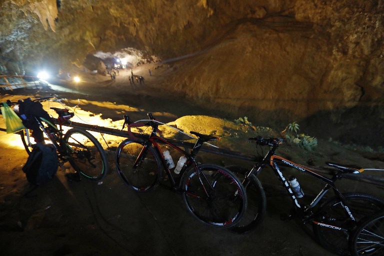 RESCUE OPS. Bicycles belonging to members of a children's football team, who are trapped in a cave chamber along with their coach, are seen as Thai rescue personnel (background) conduct operations under floodlights at the entrance to Tham Luang cave. Photo by Krit Promsakla Na Sakolnakorn/Thai News Pix/AFP   