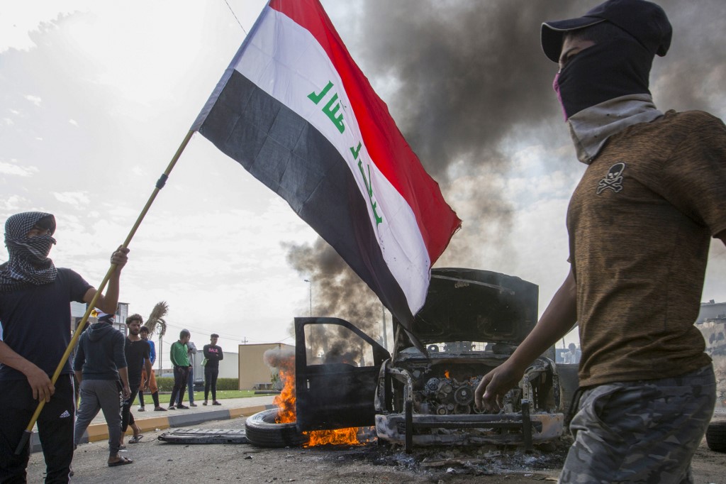 PROTESTS CONTINUE. Iraqi demonstrators stand next to the smoking remains of an Iraqi anti-riot vehicle during a demonstration in the southern city of Basra on November 24, 2019, as protesters cut-off roads and activists call for a general strike. Photo by Hussein Faleh/AFP 