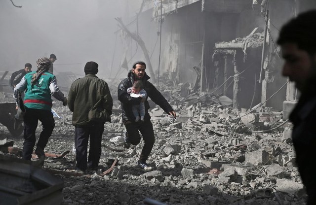 SYRIA BOMBARDMENT. A Syrian man carries an infant injured in government bombing in the rebel-held town of Hamouria, in the besieged Eastern Ghouta region on the outskirts of the capital Damascus, on February 19, 2018. File photo by Abdulmonam Eassa/AFP 