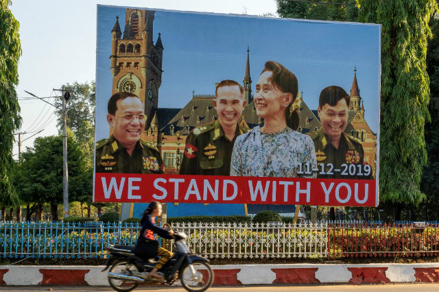 SUPPORT. In this photo taken on November 28, 2019, a woman on motorcycle rides past a huge billboard depicting Myanmar State Counsellor Aung San Su Kyi with the three military ministers with the background showing the building of the International Court of Justice in The Hague, displayed along a main road in Hpa-an, Karen State. FIle photo by AFP 