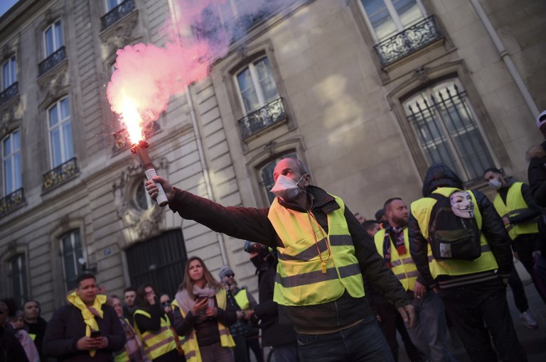 PROTEST. A man holds a flare on November 17, 2018 in Paris, during a nationwide popular initiated day of protest called "yellow vest" (Gilets Jaunes in French) movement to protest against high fuel prices which has mushroomed into a widespread protest against stagnant spending power under French President. Photo by Lucas Barioulet/AFP 
