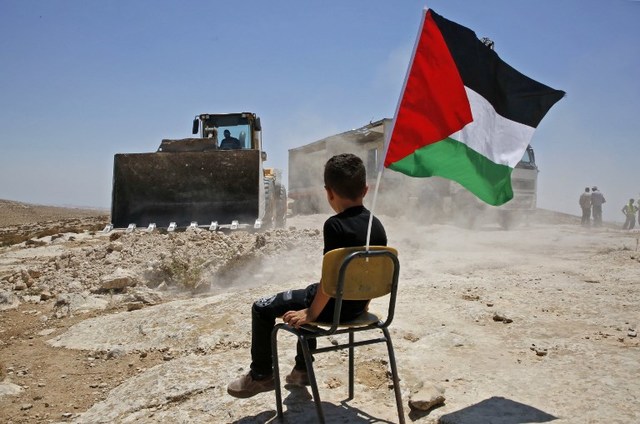 CONFLICT. A Palestinian boy sits on a chair with a national flag as Israeli authorities demolish a school site in the village of Yatta, south of the West Bank city of Hebron and to be relocated in another area, on July 11 2018. File Photo by Hazem Bader/AFP 