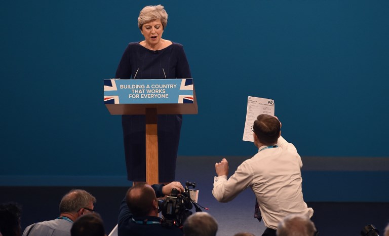 HANDING A P45. Protester comedian Simon Brodkin (R) hands a piece of paper written as a mock P45 (employee leaving form) to Britain's Prime Minister Theresa May as she was delivering her speech on the final day of the Conservative Party annual conference at the Manchester Central Convention Centre in Manchester, northwest England, on October 4, 2017. Photo by Paul Ellis/AFP 