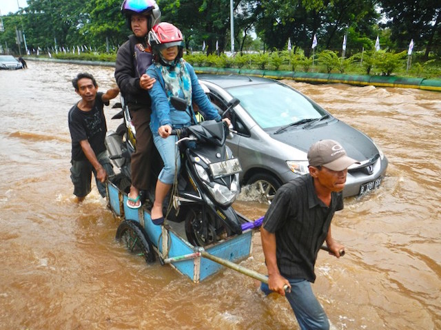 Sepasang warga Jakarta sedang duduk di atas motornya di tengah banjir. 10 Februari 2015. Foto oleh Bay Ismoyo/AFP 