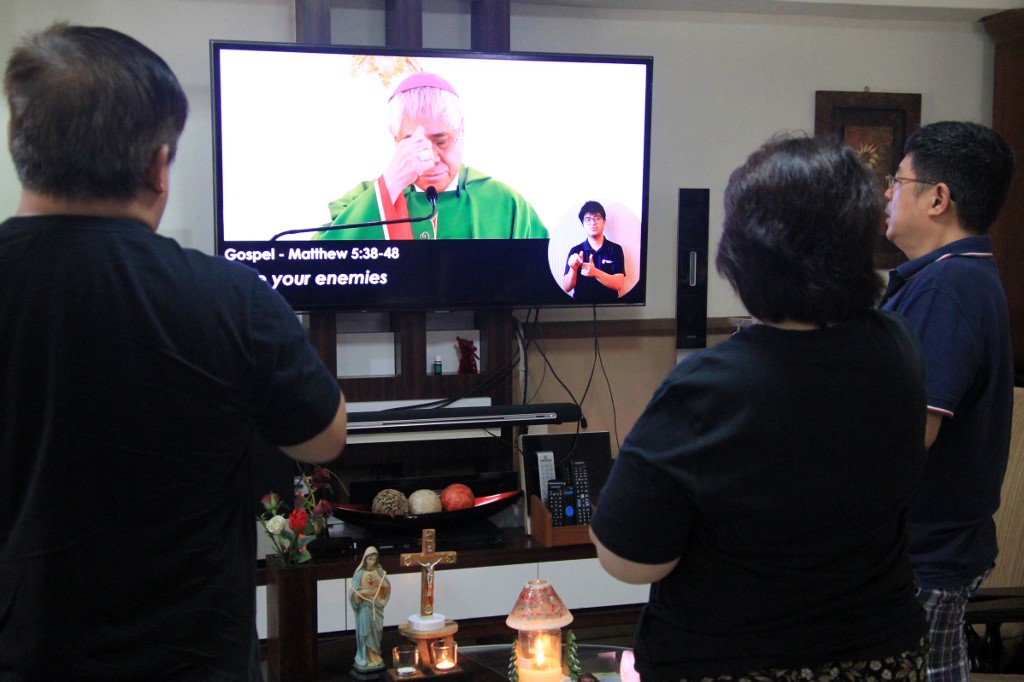 KEEPING THE FAITH. This photograph taken on February 23, 2020 shows Christian devotees listening to a pre-recorded mass by Singapore Archbishop William Goh on television inside their home as a protective measure to prevent the spread of the COVID-19 coronavirus in Singapore. Photo by Martin Abbugao/AFP 