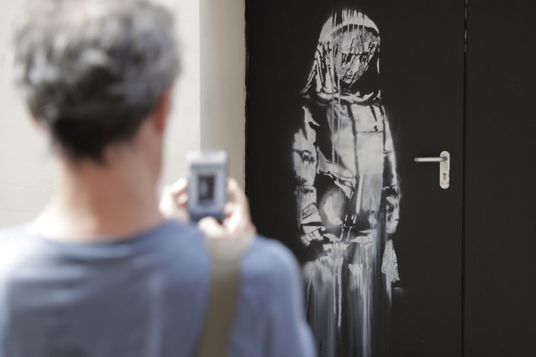 STREET ART. A man takes a photograph of a recent artwork by street artist Banksy in Paris on June 25, 2018, on a side street to the Bataclan concert hall where a terrorist attack killed 90 people on Novembre 13, 2015. Photo by Thomas SAMSON / AFP 