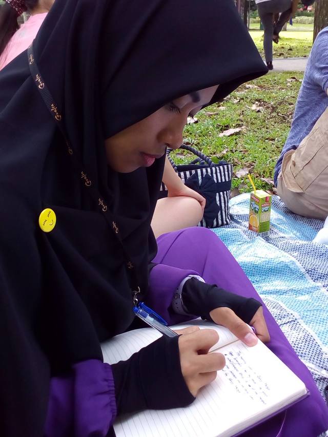 Seorang buruh migran asal Indonesia menulis puisi di sebuah taman di Singapura. Foto oleh Voices of Singapore’s Invisible Hands