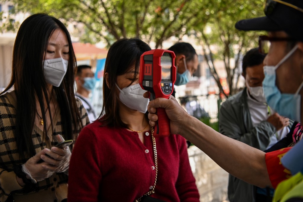 CHECK. A worker wearing a face mask checks passengers body temperatures and a health code on their phones in Wuhan, China's central Hubei province on May 12, 2020. Photo by Hector Retamal/AFP 