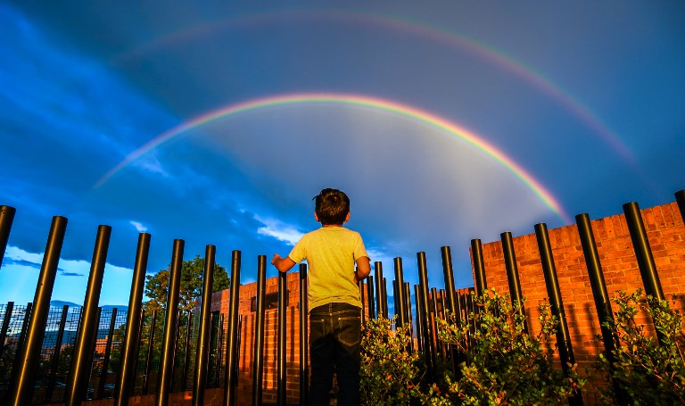 DUSK. A boy looks at a rainbow during a sunset in Bogota, Colombia on December 13, 2017. Photo by Luis Acosta/AFP 