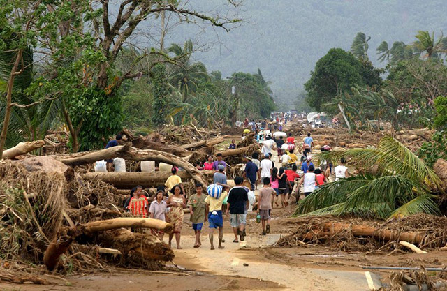 Villagers looking for relief goods pass the General Nakar to Infanta highway in Quezon province partly cleared with logs 07 December 2004. Flash floods carrying debris of logs and earth washed down from nearby Sierra Madre mountain range made roads impassable to vehicles and turned farms and villages into wasteland. Thousands were left homeless and over 1,400 dead and missing from the two storms that rampaged in the northeastern Philippines in one week. President Gloria Arroyo earlier ordered the suspension of commercial logging in the area after resident blamed the disaster on illegal loggers. Photo by AFP/Romeo Gacad 