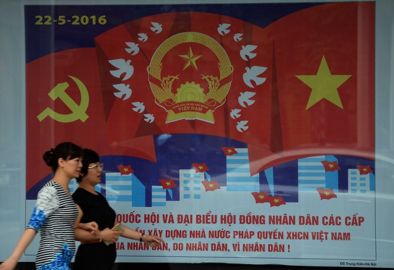 JUST AN ACT? This picture taken on April 21, 2016 shows people walking past a propaganda poster featuring the upcoming legislative elections in downtown Hanoi. File photo by Hoang Dinh Nam/AFP 