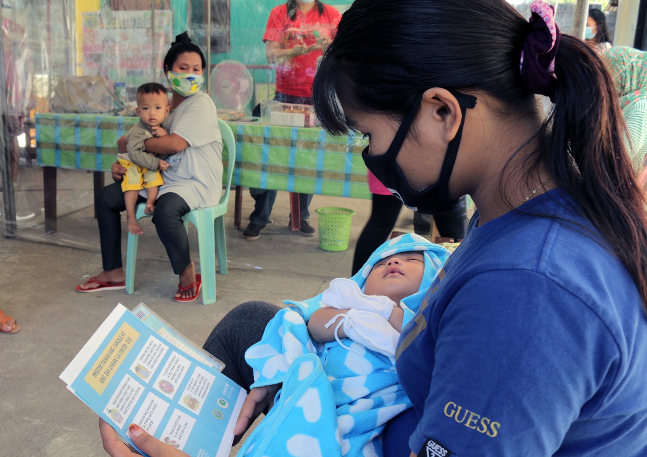 A mother in Maguindanao reads a COVID-19 leaflet as she waits for her child to be vaccinated. Photo from Unicef 