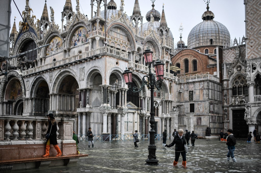 FLOODED. Pedestrians walk across the flooded St. Mark's Square past St. Mark's Basilica after an exceptional overnight high tide water level, on November 13, 2019 in Venice. Photo by Marco Bertorello/AFP 