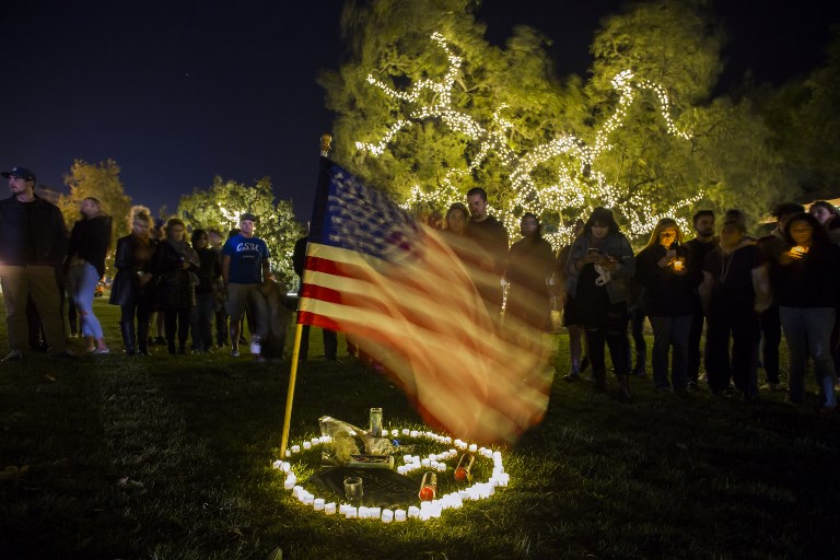 TRIBUTE. People stand around candles in the grass next to a US flag during a vigil to pay tribute to the victims of a shooting in Thousand Oaks, California, on November 8, 2018. Photo by Apu Gomes/AFP  