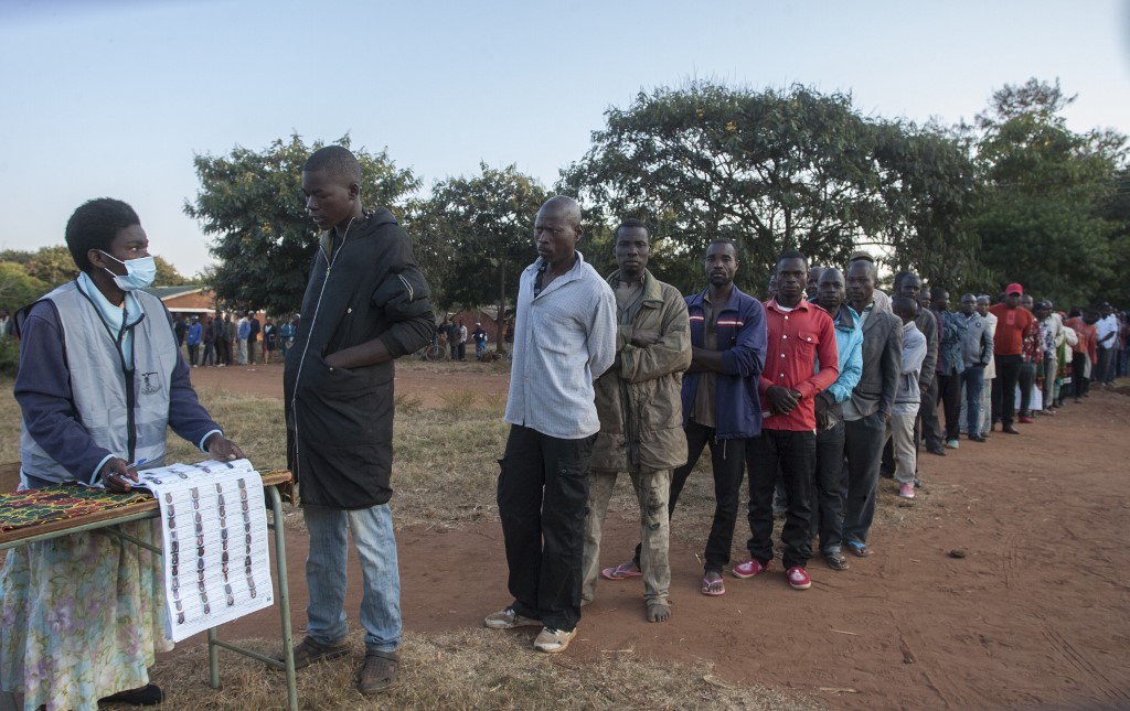 RERUN. An electoral official (L) checks the voters' roll while people queue to vote at the Malembo polling station during the presidential elections in Lilongwe on June 23, 2020. Photo by Amos Gumulira/AFP 