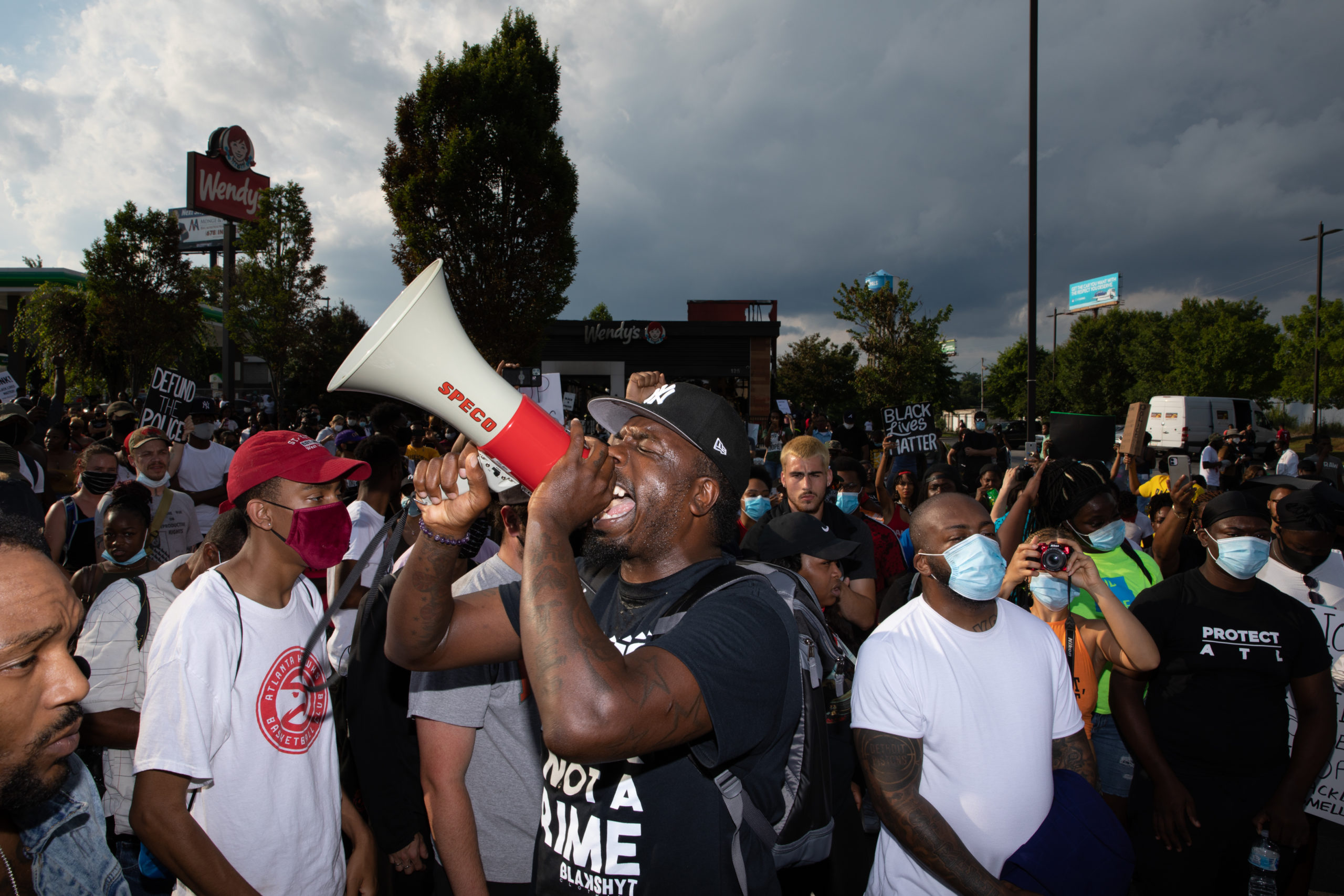 PROTEST. A man speaks into a bull-horn in front of the Wendy's restaurant set ablaze overnight on June 14, 2020 in Atlanta, Georgia. Rayshard Brooks, 27, was shot and killed yesterday by police in a struggle following a field sobriety test at the Wendy's. Photo by Dustin Chambers/Getty Images for Coda Story. 