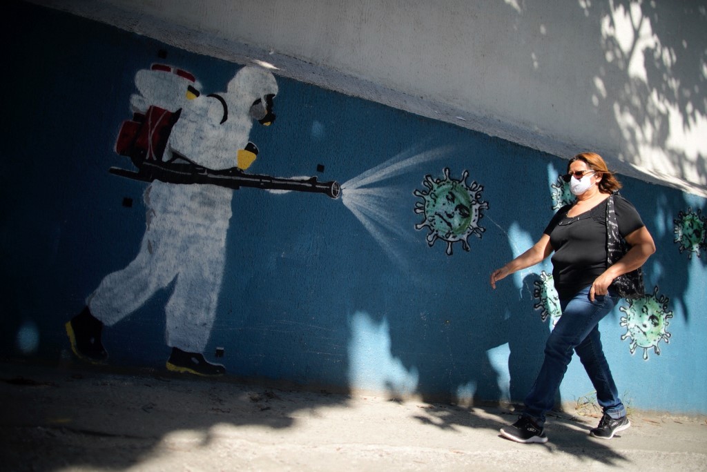 IMMUNITY? A woman walks in front of a mural depicting a person in a protective suit spraying disinfectant on a coronavirus in Rio de Janeiro, Brazil on July 8, 2020. Photo by Mauro Pimentel/AFP 