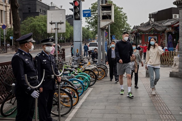 INVESTIGATION? Police officers (L) secure an area as people wearing face masks as a preventive measure against the COVID-19 coronavirus walk on a street in Beijing on May 4, 2020. File photo by Nicolas Asfouri / AFP 