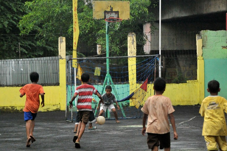 Anak-anak di sebuah lapangan di bawah lintasan rel kereta api di Jakarta sedang memainkan si kulit bundar. Foto oleh Bay Ismoyo/AFP
